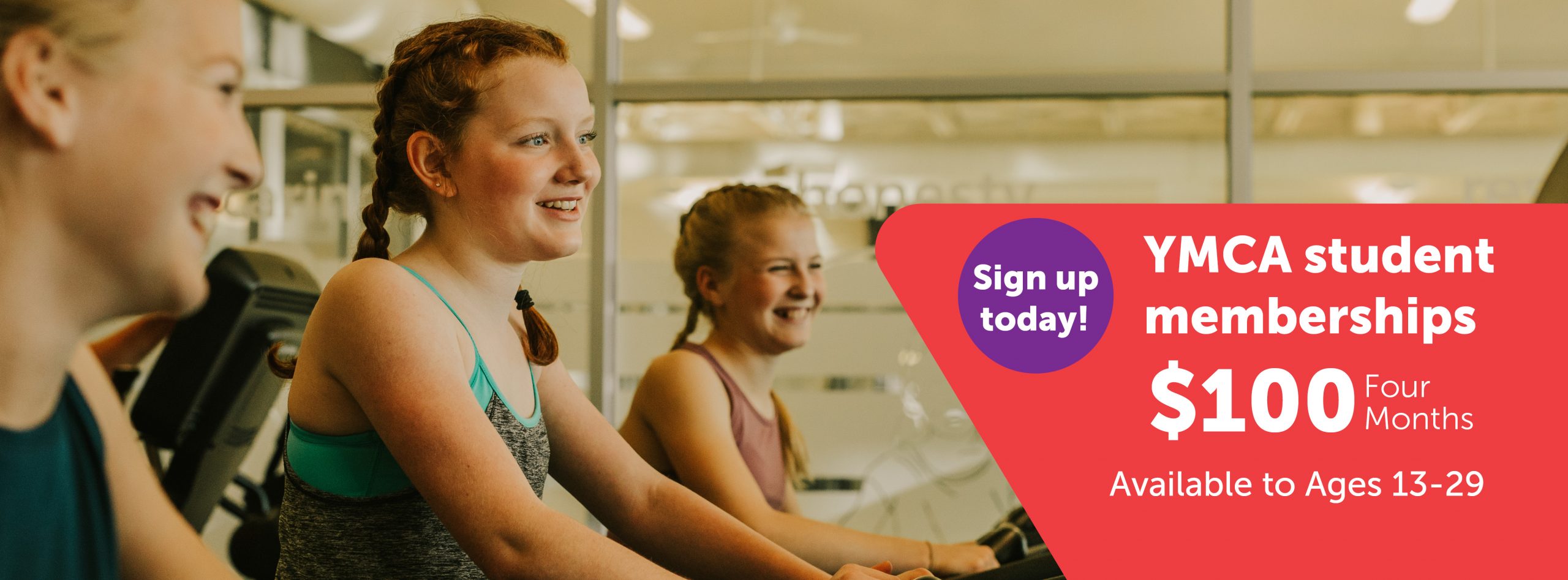 Three young people are exercising on cardio equipment at a YMCA fitness centre, smiling and enjoying their workout. A promotional banner on the right reads: “Sign up today! YMCA student memberships – $100 for four months. Available to ages 13–29.” The ad promotes a discounted YMCA membership offer for students and young adults.